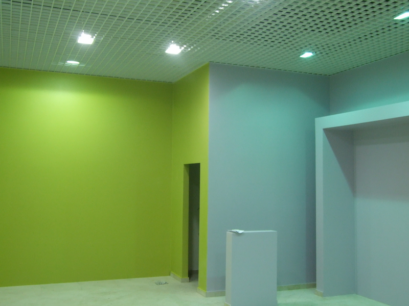 Wnętrze biura po malowaniu ścian na zielono i szaro, z podwieszanym sufitem rastrowym i minimalistycznym postumentem.